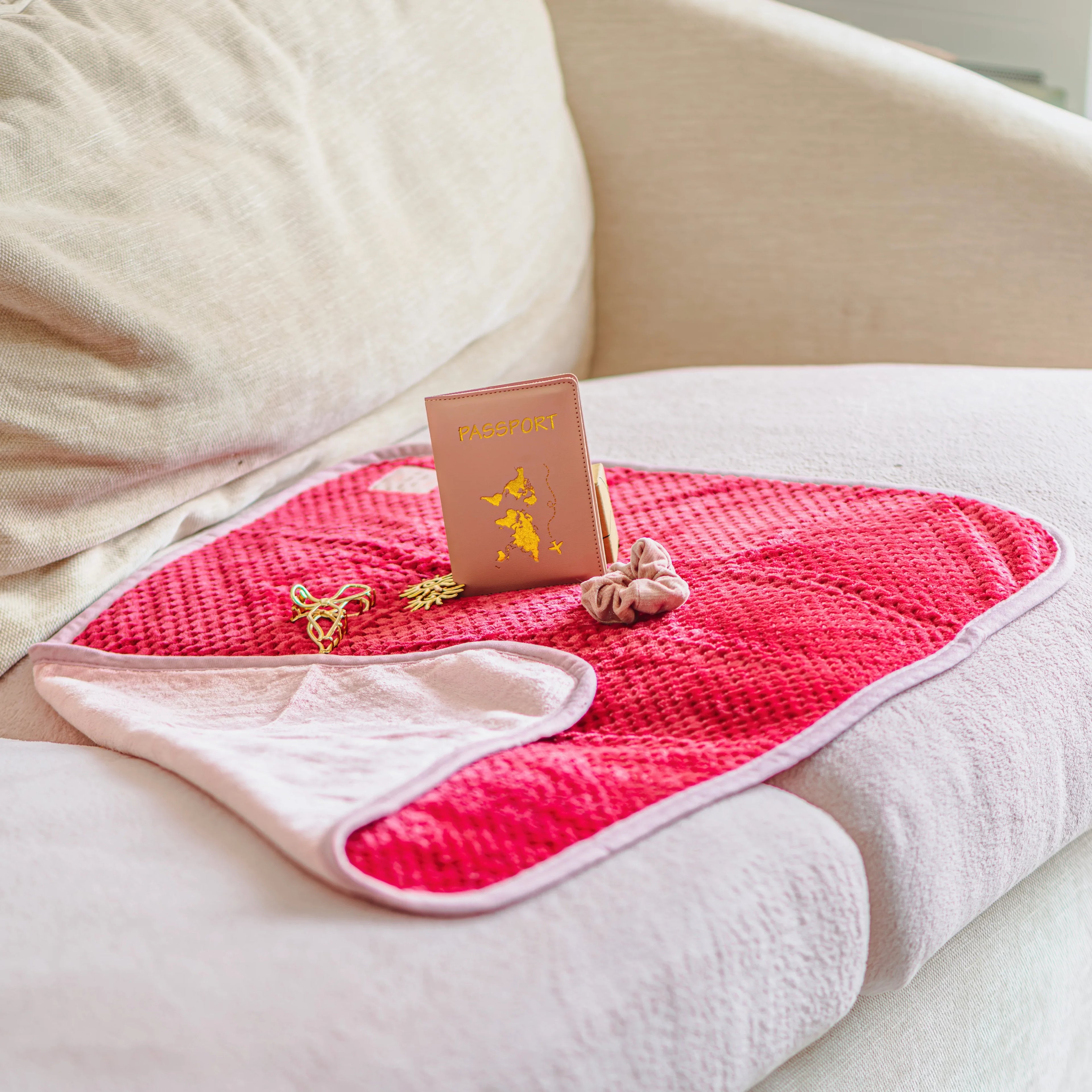 Plaid imperméable rose avec passeport et accessoires sur canapé, idéal pour confort et praticité